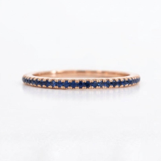 A rose gold eternity ring featuring a continuous row of round-cut deep blue sapphires, shown on a clean white background.