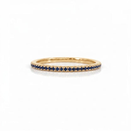 A delicate yellow gold eternity ring featuring a single row of round-cut deep blue sapphires, set against a clean white background.