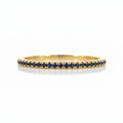 A thin yellow gold eternity ring set with a single row of round-cut deep blue sapphires, shown on a clean white background with a soft reflection.