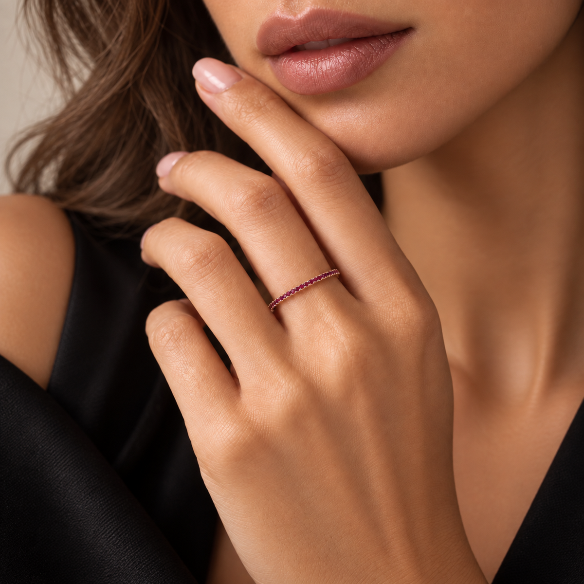 A close-up lifestyle shot of a model wearing a delicate, thin rose band ring set with small, closely-set red rubies on her ring finger.