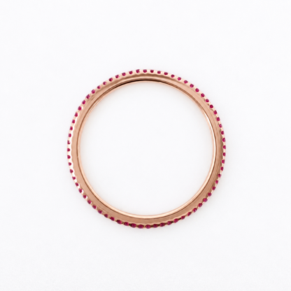 A rose gold bangle bracelet with a row of small red gemstones set along the outer edge, shown against a plain white background.