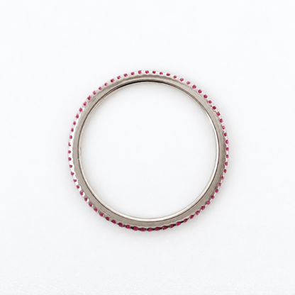 A silver-toned circular ring with a border of small, evenly spaced red gemstones, photographed on a clean white background.