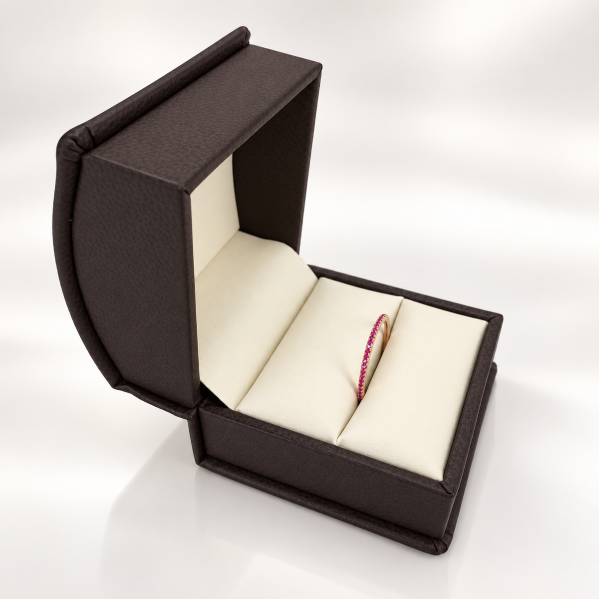 An open dark brown textured jewelry box with cream-colored interior cushions, showcasing a single red ruby band ring inside.