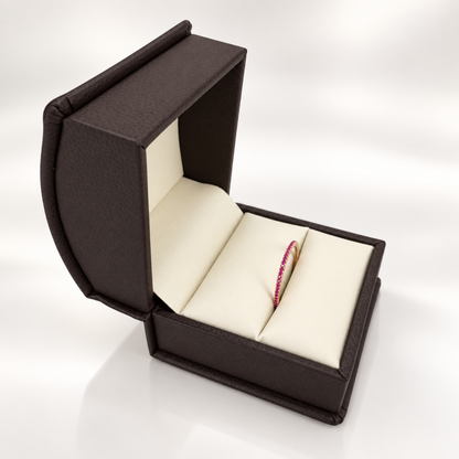 An open dark brown textured jewelry box with cream-colored interior cushions, showcasing a single red ruby band ring inside.