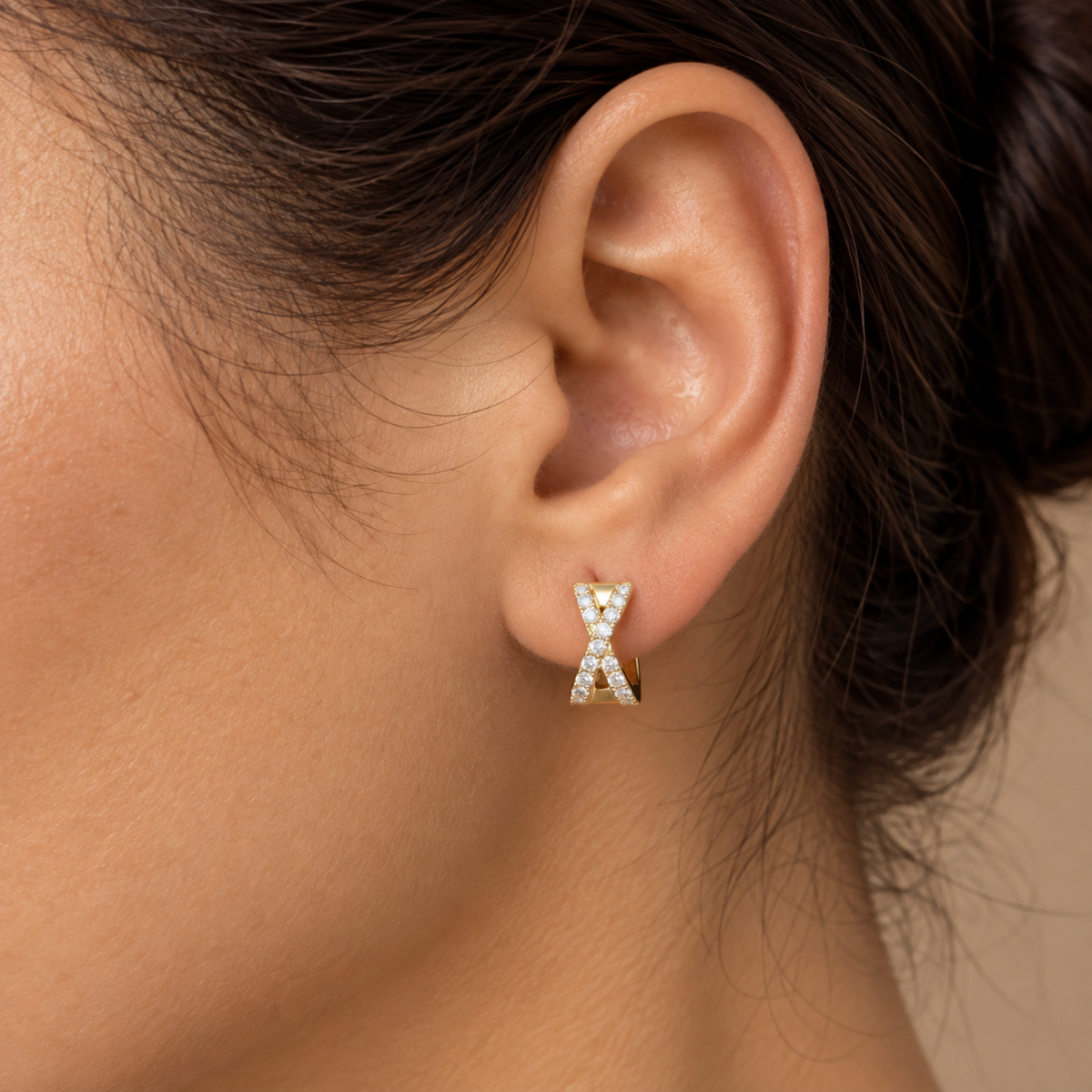 Close-up of a solid 14K yellow gold natural diamond X huggie earring worn on the ear, highlighting the X-shaped design and round diamond settings.