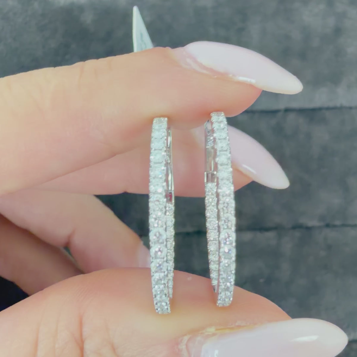 Video of a hand holding 1-inch natural diamond inside-out hoop earrings in solid 18K white gold, showing the round brilliant diamonds.
